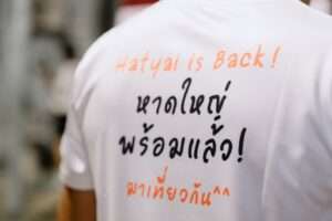 ภาพถ่ายเจาะจงที่ด้านหลังเสื้อของนักวิ่ง ซึ่งสกรีนข้อความชวนเที่ยว Hatyai is Back! หาดใหญ่พร้อมแล้ว! มาเที่ยวกัน