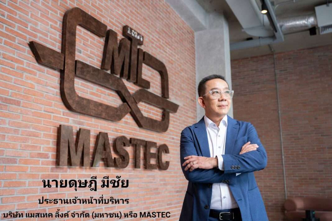 นายดุษฎี มีชัย ประธานเจ้าหน้าที่บริหาร บริษัท แมสเทค ลิ้งค์ จำกัด (มหาชน) หรือ MASTEC ยืนกอดอกด้วยความมั่นใจ ถ่ายภาพคู่กับโลโก้บริษัท