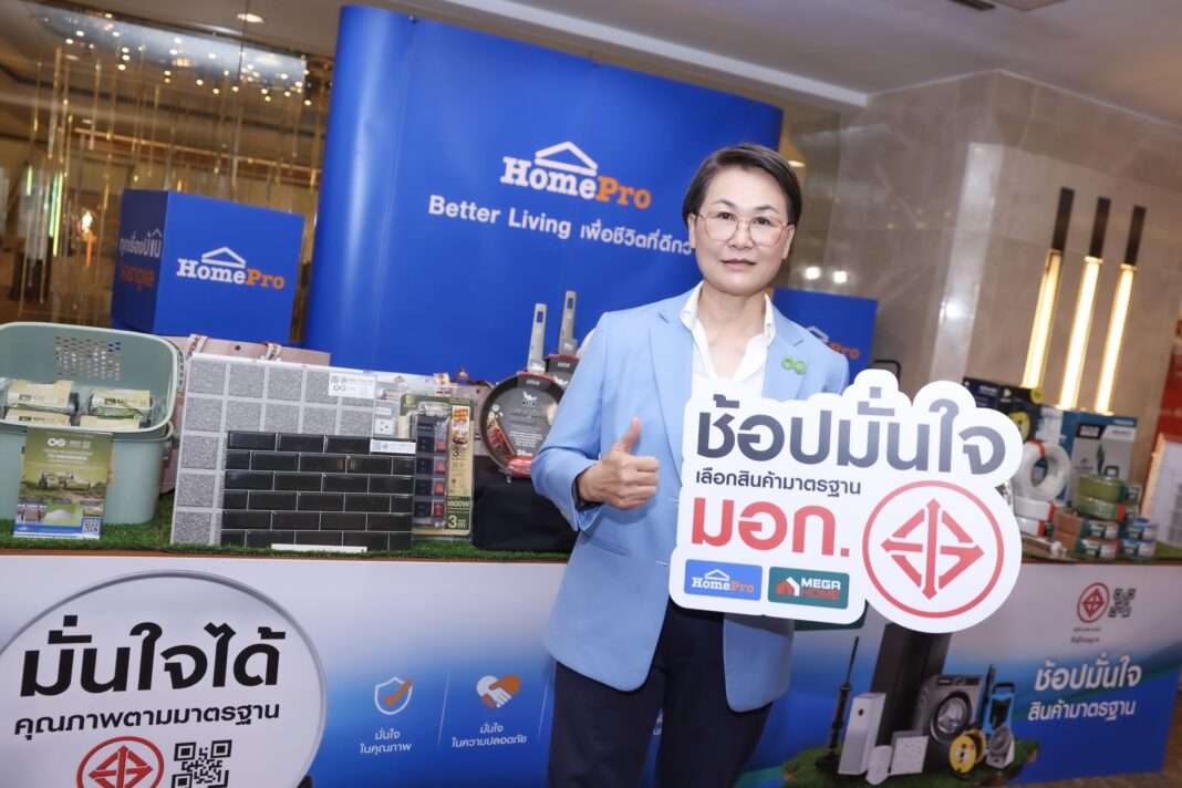 ผู้บริหารหญิงจากโฮมโปรถ่ายภาพร่วมกับป้ายแคมเปญช้อปมั่นใจเลือกสินค้ามาตรฐาน มอก. พร้อมจัดแสดงสินค้าที่ผ่านการรับรอง
