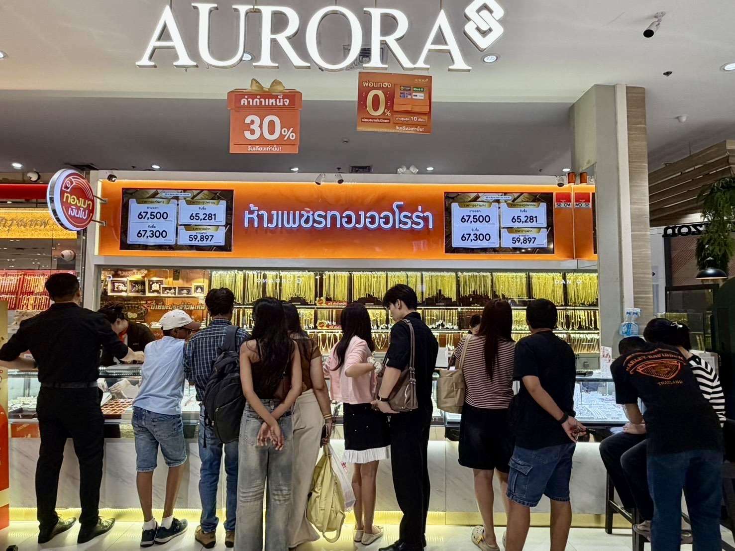 ภาพบรรยากาศบริเวณหน้าร้านห้างเพชรทองออโรร่า มีกลุ่มลูกค้าจำนวนมากกำลังยืนเลือกชมและซื้อสินค้าทองคำและเครื่องประดับที่หน้าเคาน์เตอร์