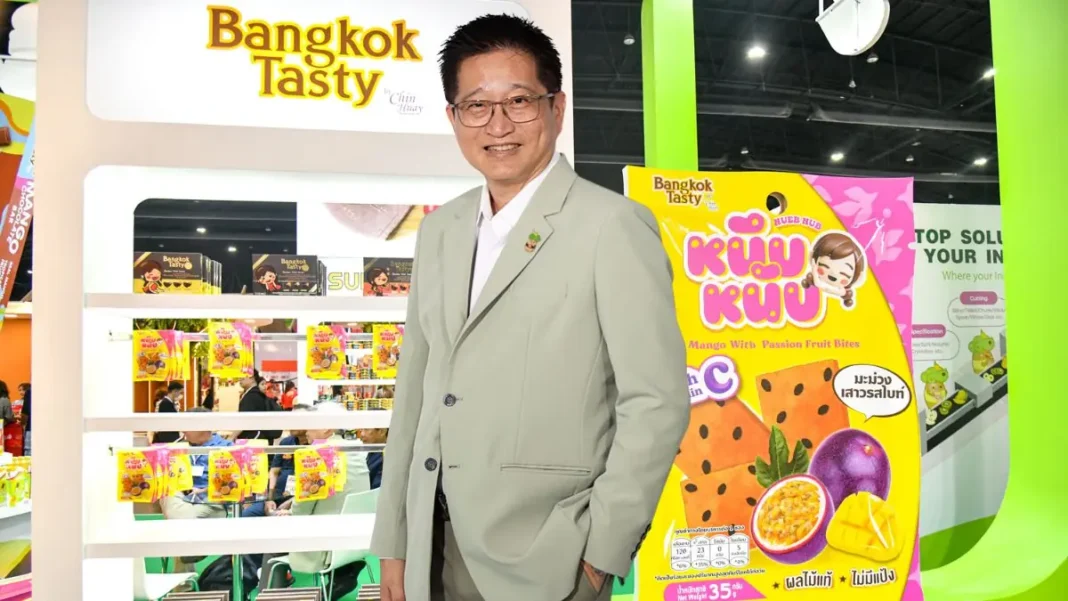 Prawit-Srisaengnam-CEO-CH-Charoen-Industry-Bangkok-Tasty ภาพนายประวิทย์ ศรีแสงนาม ประธานเจ้าหน้าที่บริหาร บริษัท เจริญอุตสาหกรรม จำกัด (มหาชน) หรือ CH สวมสูทสีเทา ยืนยิ้มถ่ายภาพคู่กับบูธแสดงสินค้าแบรนด์ Bangkok Tasty และผลิตภัณฑ์มะม่วงเสาวรสหนึบหนับ