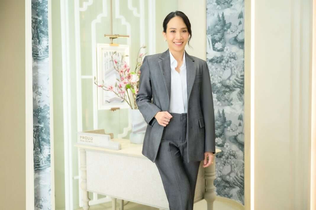 Prouputh-Liptapanlop-Executive-Director-PROUD-Real-Estate ภาพนางสาวพราวพุธ ลิปตพัลลภ กรรมการบริหาร บริษัท พราว เรียล เอสเตท จำกัด (มหาชน) หรือ PROUD สวมชุดสูทสีเทา ยืนยิ้มถ่ายภาพในพื้นที่ตกแต่งหรูหรา เพื่อนำเสนอความสำเร็จของโครงการ The Residences at InterContinental Phuket Resort