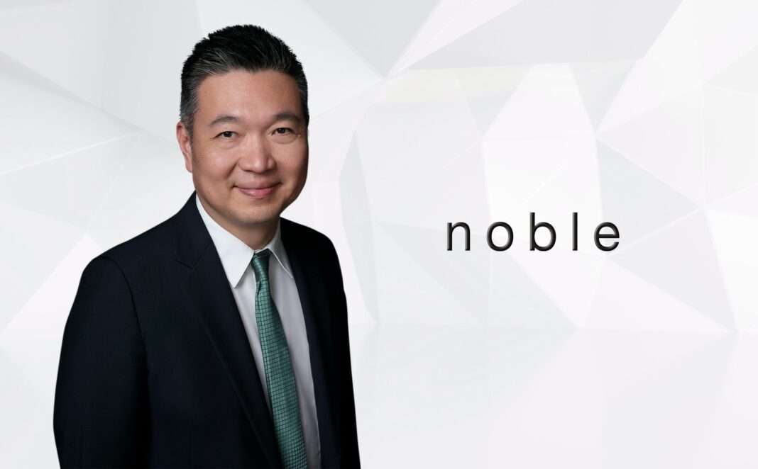 Thongchai-Busrapan-Co-CEO-Noble-Development-Q2-2026 ภาพนายธงชัย บุศราพันธ์ รองประธานกรรมการและประธานเจ้าหน้าที่บริหารร่วม บริษัท โนเบิล ดีเวลลอปเมนท์ จำกัด (มหาชน) สวมชุดสูทสีกรมท่า ยืนยิ้มถ่ายภาพคู่กับโลโก้ noble
