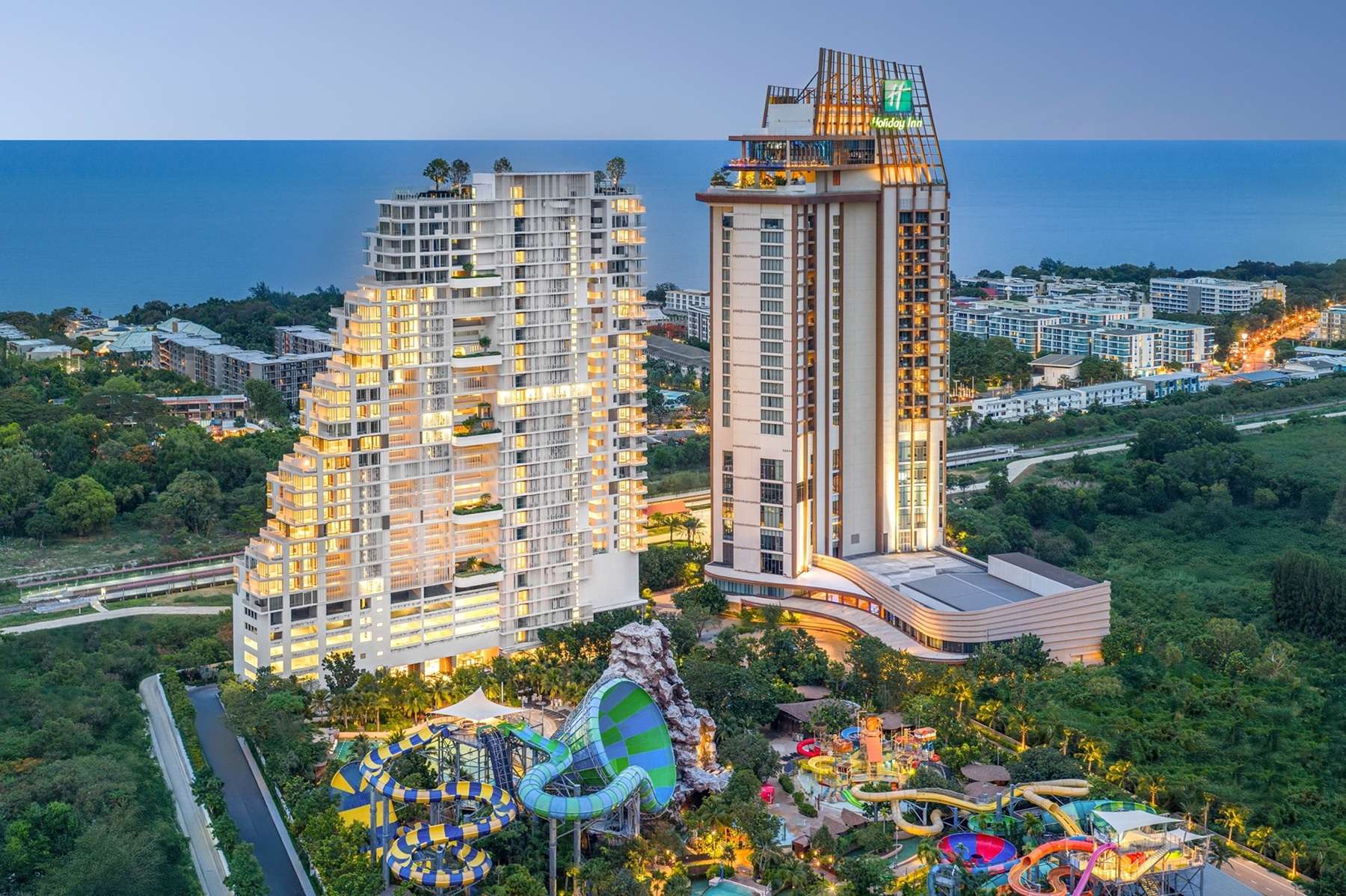ภาพทัศนียภาพมุมสูงของโครงการคอนโดมิเนียม VEHHA Hua Hin (เวหา หัวหิน) ตึกสูงสีขาวดีไซน์ทันสมัย ตั้งตระหง่านคู่กับโรงแรมฮอลิเดย์ อินน์ วานา นาวา หัวหิน โดยมีฉากหลังเป็นวิวทะเลและสวนน้ำวานา นาวา