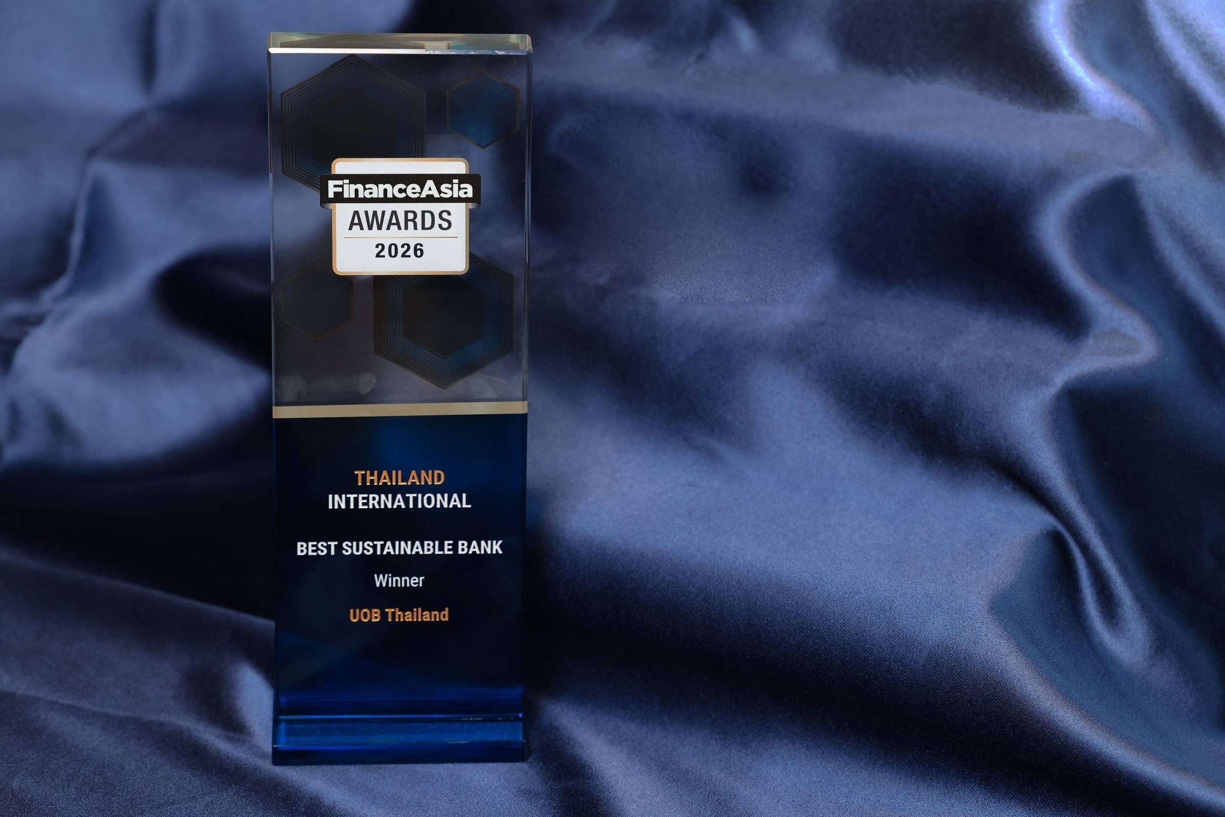 ภาพถ้วยรางวัลเกียรติยศ FinanceAsia Awards 2026 สาขา Best Sustainable Bank (International) 2026 ที่มอบให้แก่ธนาคารยูโอบี ประเทศไทย วางโดดเด่นบนพื้นหลังผ้าสีน้ำเงิน