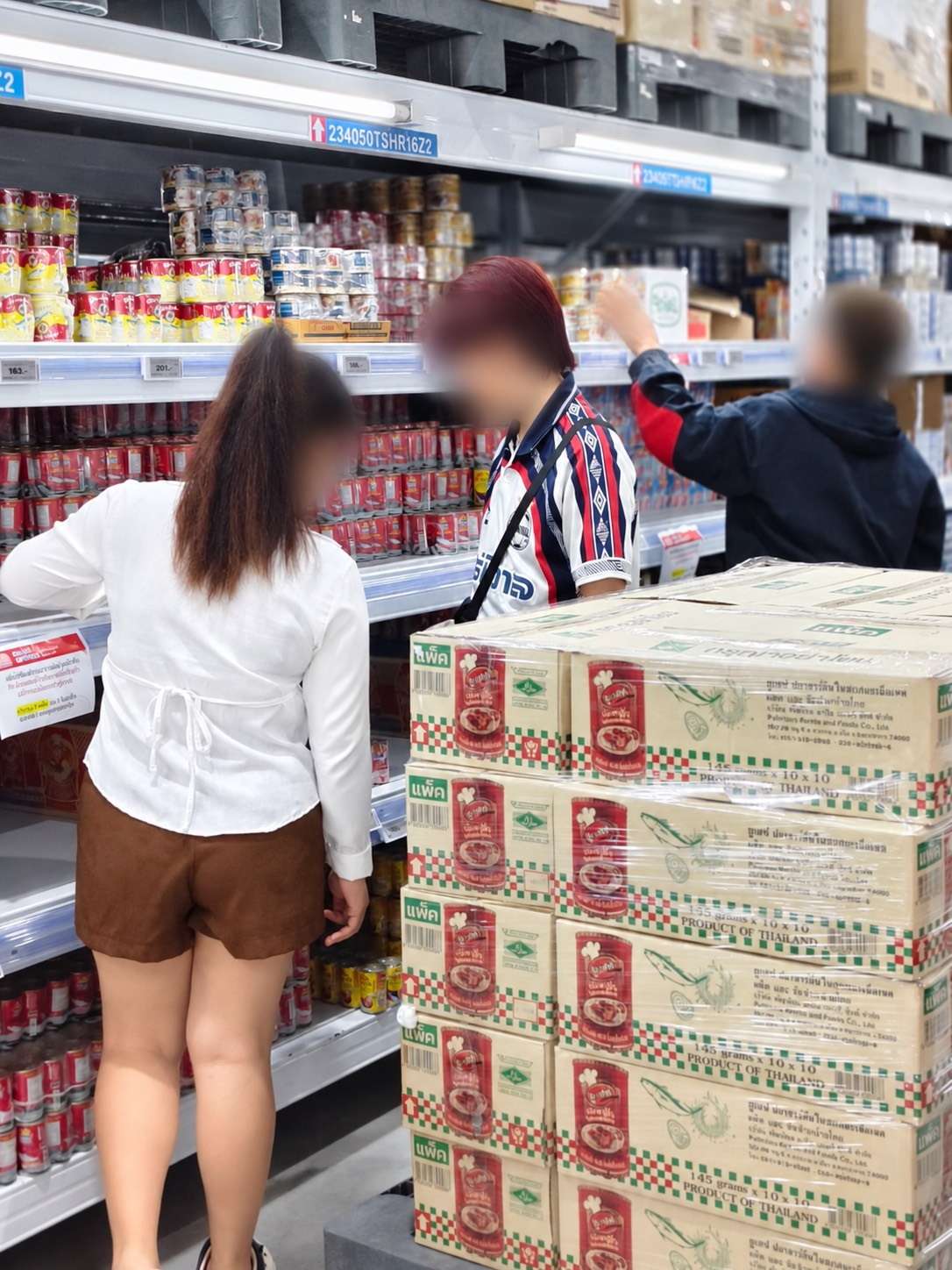ภาพลูกค้ากำลังเลือกซื้อสินค้าประเภทอาหารกระป๋องบนชั้นวางภายในศูนย์ค้าส่ง โก โฮลเซลล์ (GO WHOLESALE) โดยมีสต็อกสินค้าจัดเตรียมไว้อย่างเต็มพิกัดเพื่อพร้อมให้บริการ
