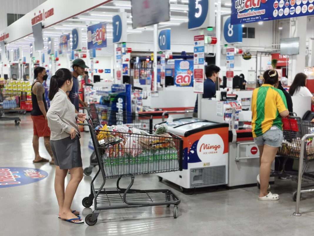 GO-WHOLESALE-Customers-Checkout-Counter-Stock-Preparation ภาพบรรยากาศลูกค้ากำลังต่อคิวชำระเงินที่จุดแคชเชียร์ภายในศูนย์ค้าส่ง โก โฮลเซลล์ (GO WHOLESALE) โดยมีรถเข็นที่เต็มไปด้วยสินค้าอุปโภคบริโภคและวัตถุดิบอาหาร เพื่อเตรียมความพร้อมในช่วงสถานการณ์น้ำท่วม