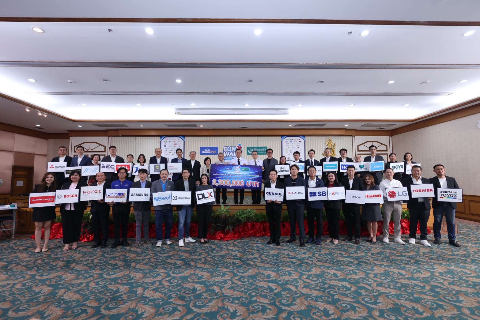 ภาพหมู่ผู้บริหารโฮมโปร คณะแพทย์จากโรงพยาบาลศิริราช และตัวแทนพันธมิตรทางธุรกิจที่ถือป้ายโลโก้แบรนด์ต่างๆ ร่วมถ่ายภาพเป็นที่ระลึกอย่างพร้อมเพรียงบนเวทีในงานส่งมอบเงินบริจาค