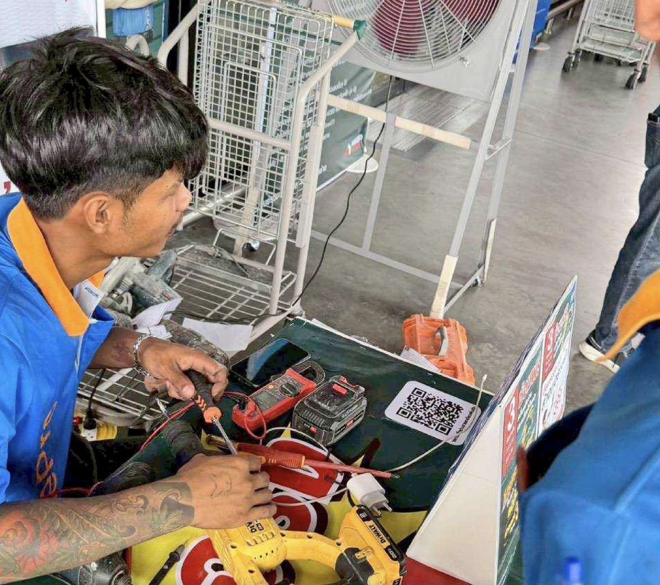 ภาพช่างจากทีม CHANG HomePro กำลังมุ่งมั่นตรวจสอบและซ่อมแซมเครื่องมือช่างสว่านไฟฟ้าสีเหลืองให้แก่ลูกค้าที่นำมาเข้ารับบริการภายในงานกิจกรรมซ่อมฟรี ณ สาขาโฮมโปร