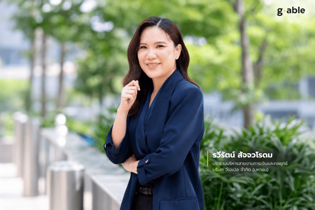 Raweerat-Satjawarodom-CFO-G-Able-Economy-Of-Speed-AI ภาพคุณรวีรัตน์ สัจจวโรดม ประธานบริหารสายงานการเงินและกลยุทธ์ บริษัท จีเอเบิล จำกัด (มหาชน) หรือ GABLE สวมชุดสูทสีน้ำเงิน ยืนกอดอกถ่ายภาพด้วยความมั่นใจบริเวณพื้นที่สีเขียวภายนอกอาคาร