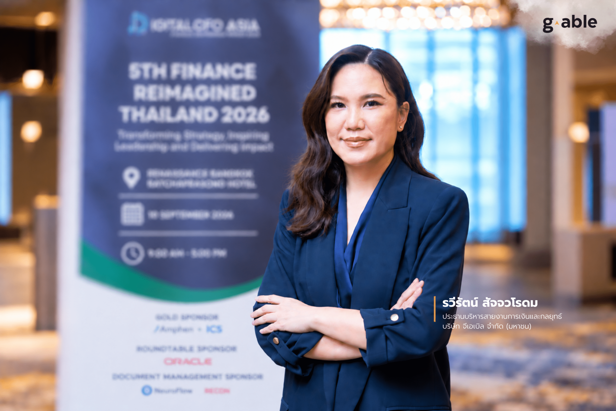 ภาพคุณรวีรัตน์ สัจจวโรดม ประธานบริหารสายงานการเงินและกลยุทธ์ บริษัท จีเอเบิล จำกัด (มหาชน) ยืนกอดอกถ่ายภาพหน้าป้ายงานสัมมนา 5TH FINANCE REIMAGINED THAILAND 2026