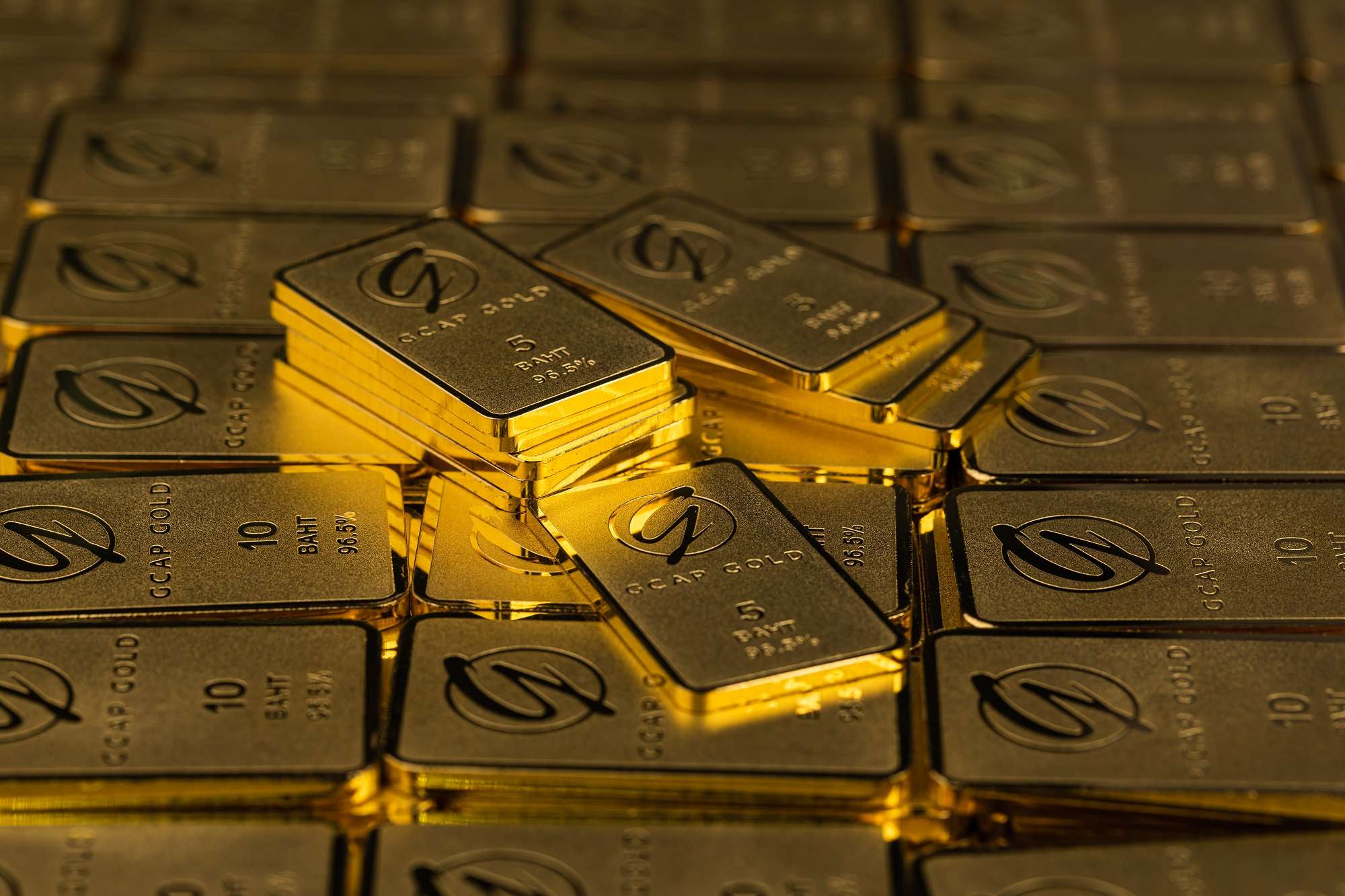 ภาพทองคำแท่งสลักโลโก้ GCAP GOLD น้ำหนัก 5 บาท และ 10 บาท จัดเรียงซ้อนกันอย่างสวยงาม สะท้อนความมั่งคั่งและโอกาสในการลงทุน
