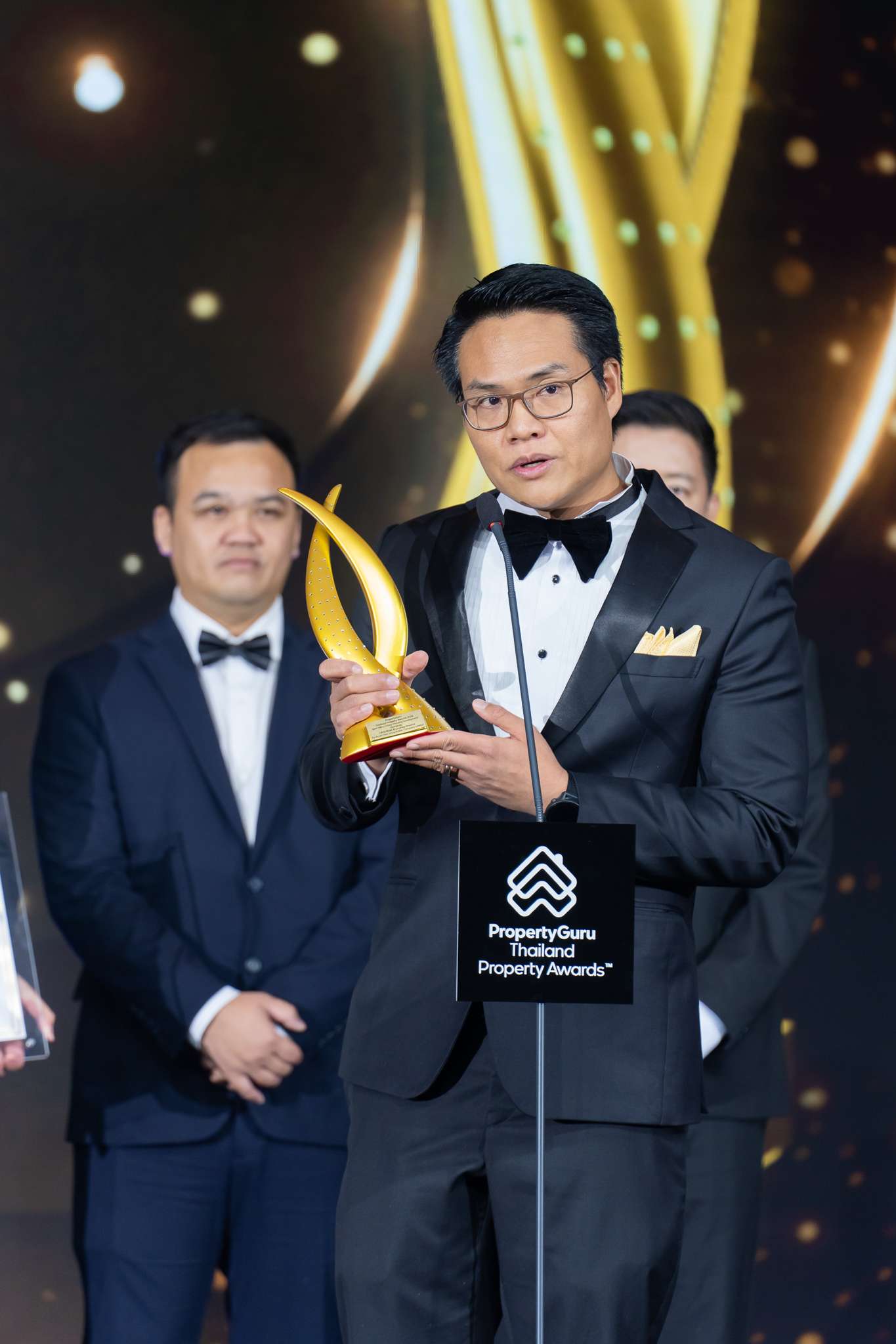 ภาพนายศุภโชค ปัญจทรัพย์ ประธานเจ้าหน้าที่บริหาร บริษัท แอสเซท ไฟว์ กรุ๊ป จำกัด (มหาชน) หรือ A5 สวมชุดทักซิโด้ ยืนถือถ้วยรางวัลสีทองและกล่าวสุนทรพจน์บนเวทีงาน PropertyGuru Thailand Property Awards 2026