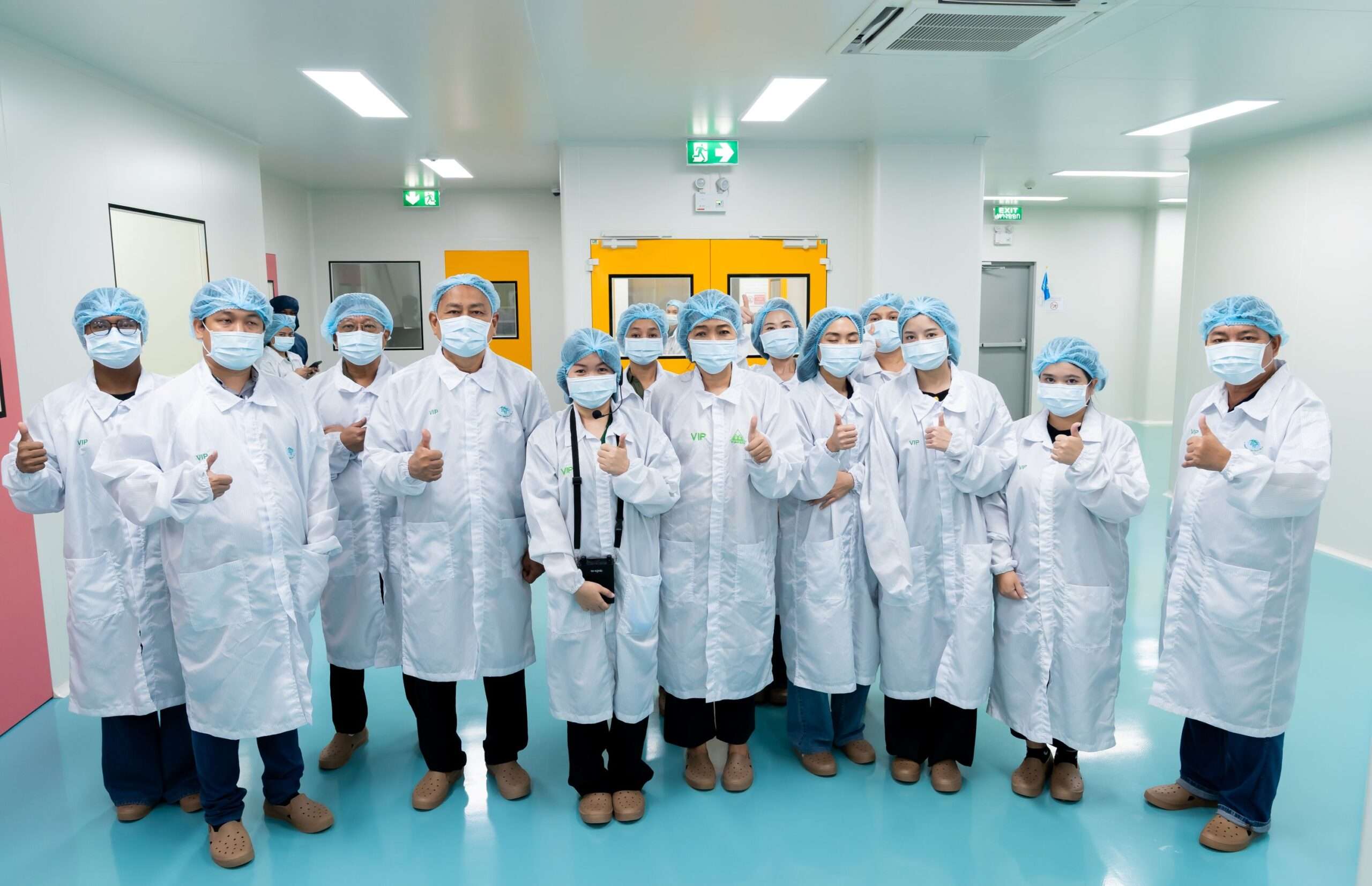 ภาพคณะสื่อมวลชนและผู้บริหารสวมชุดคลุมปฏิบัติการไร้ฝุ่นสีขาว (Cleanroom Suit) พร้อมหมวกและหน้ากากอนามัย ถ่ายภาพหมู่ร่วมกันชูนิ้วโป้งแสดงความเยี่ยมยอดภายในพื้นที่โรงงานเฮเว่น เฮิร์บ