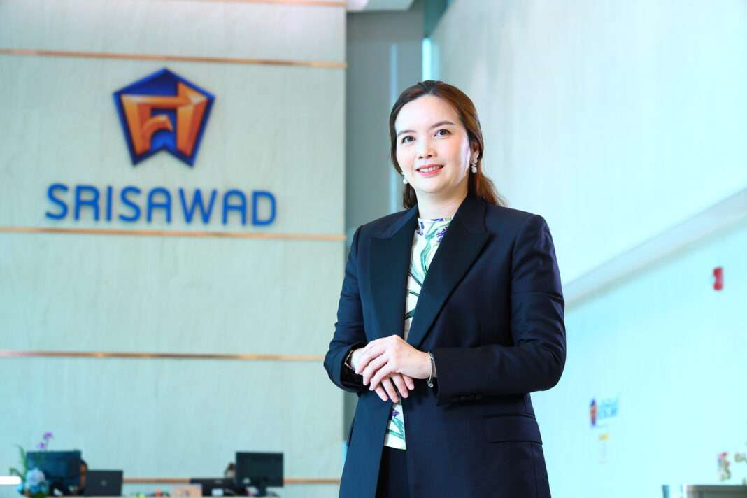 ภาพนางสาวธิดา แก้วบุตตา ผู้อำนวยการฝ่ายกลยุทธ์องค์กร บริษัท ศรีสวัสดิ์ คอร์ปอเรชั่น จำกัด (มหาชน) หรือ SAWAD สวมชุดสูทสีกรมท่ายืนด้วยความมั่นใจบริเวณหน้าโลโก้บริษัท เพื่อประกาศมติที่ประชุมคณะกรรมการบริษัทในการจ่ายเงินปันผลระหว่างกาล