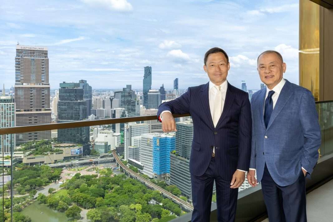 ภาพคุณชาญศักดิ์ เฟื่องฟู กรรมการรองผู้จัดการใหญ่ ธนาคารกรุงเทพ จำกัด (มหาชน) และคุณสรพจน์ เตชะไกรศรี ผู้พัฒนาโครงการนิมิต ลุมพินี พาร์ค นอร์ท สวมชุดสูทสากล ถ่ายภาพร่วมกันบริเวณระเบียงห้องพักหรูที่มองเห็นวิวสวนลุมพินีและตึกสูงตระหง่านใจกลางกรุงเทพฯ
