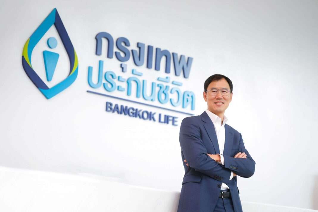 Chone-Sophonpanich-CEO-Bangkok-Life-Assurance-BLA-Pension-888 นายโชน โสภณพนิช กรรมการผู้จัดการใหญ่และประธานเจ้าหน้าที่บริหาร บริษัท กรุงเทพประกันชีวิต จำกัด (มหาชน) สวมชุดสูทสีกรมท่ายืนกอดอกด้วยความมั่นใจ ด้านหน้าป้ายโลโก้บริษัท กรุงเทพประกันชีวิต