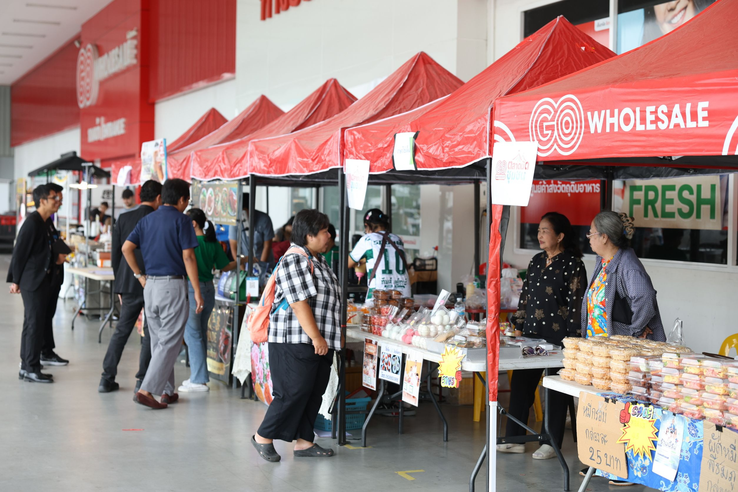 บรรยากาศโครงการ ‘ตลาดนัดชุมชน’ บริเวณหน้าสาขาโก โฮลเซลล์ มีเต็นท์สีแดงตั้งเรียงรายให้ผู้ประกอบการ SMEs นำสินค้ามาวางจำหน่าย โดยมีลูกค้าเดินเลือกซื้อสินค้า