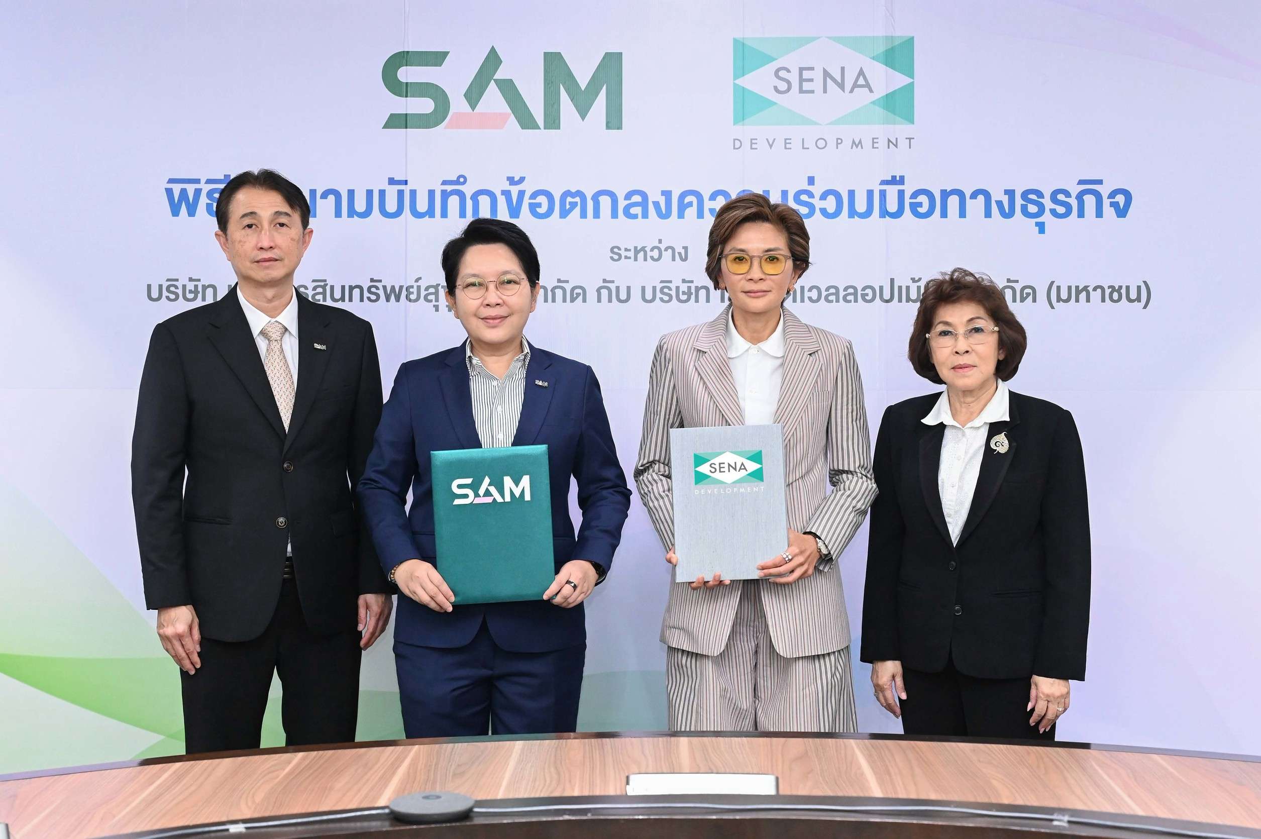 ผศ.ดร.เกษรา ธัญลักษณ์ภาคย์ กรรมการผู้จัดการ SENA และ นางสาวนารถนารี รัฐปัตย์ กรรมการผู้จัดการ SAM ถือแฟ้มลงนามบันทึกข้อตกลงความร่วมมือทางธุรกิจ พร้อมด้วยคณะผู้บริหารระดับสูง