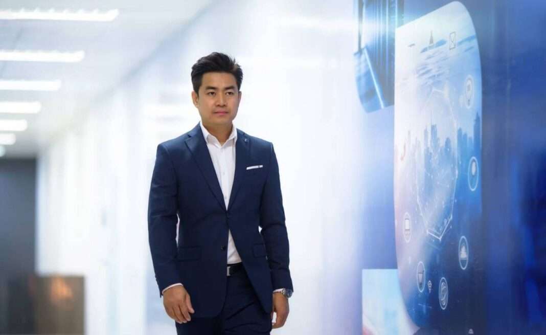 ภาพนายกิตติพันธ์ ศรีบัวเอี่ยม ประธานเจ้าหน้าที่บริหาร บริษัท โปรเอ็น คอร์ป จำกัด (มหาชน) หรือ PROEN สวมเสื้อสูทสีน้ำเงินเข้มทับเสื้อเชิ้ตสีขาว กำลังเดินอยู่บริเวณโถงทางเดินของอาคารสำนักงานที่มีการตกแต่งด้วยกราฟิกเทคโนโลยีสีฟ้า