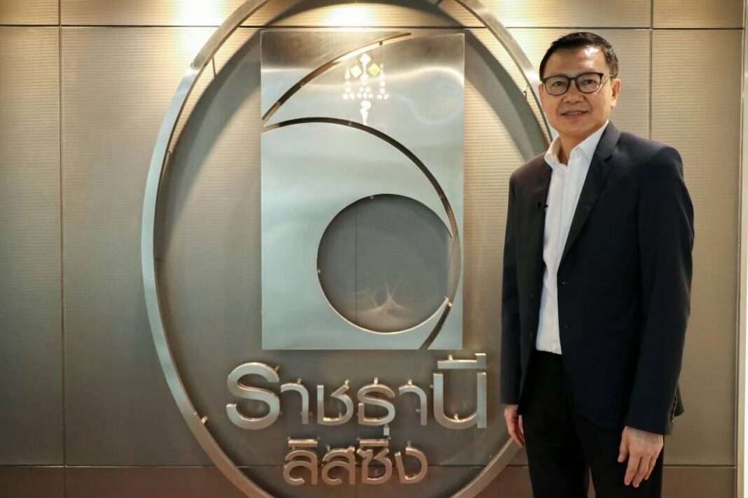 Kovit-Rungwattanasophon-Executive-Chairman-Ratchthani-Leasing นายโกวิท รุ่งวัฒนโสภณ ประธานกรรมการบริหาร บริษัท ราชธานีลิสซิ่ง จำกัด (มหาชน) หรือ THANI สวมชุดสูท ยืนถ่ายภาพด้วยความมั่นใจบริเวณด้านหน้าป้ายตราสัญลักษณ์ของบริษัท