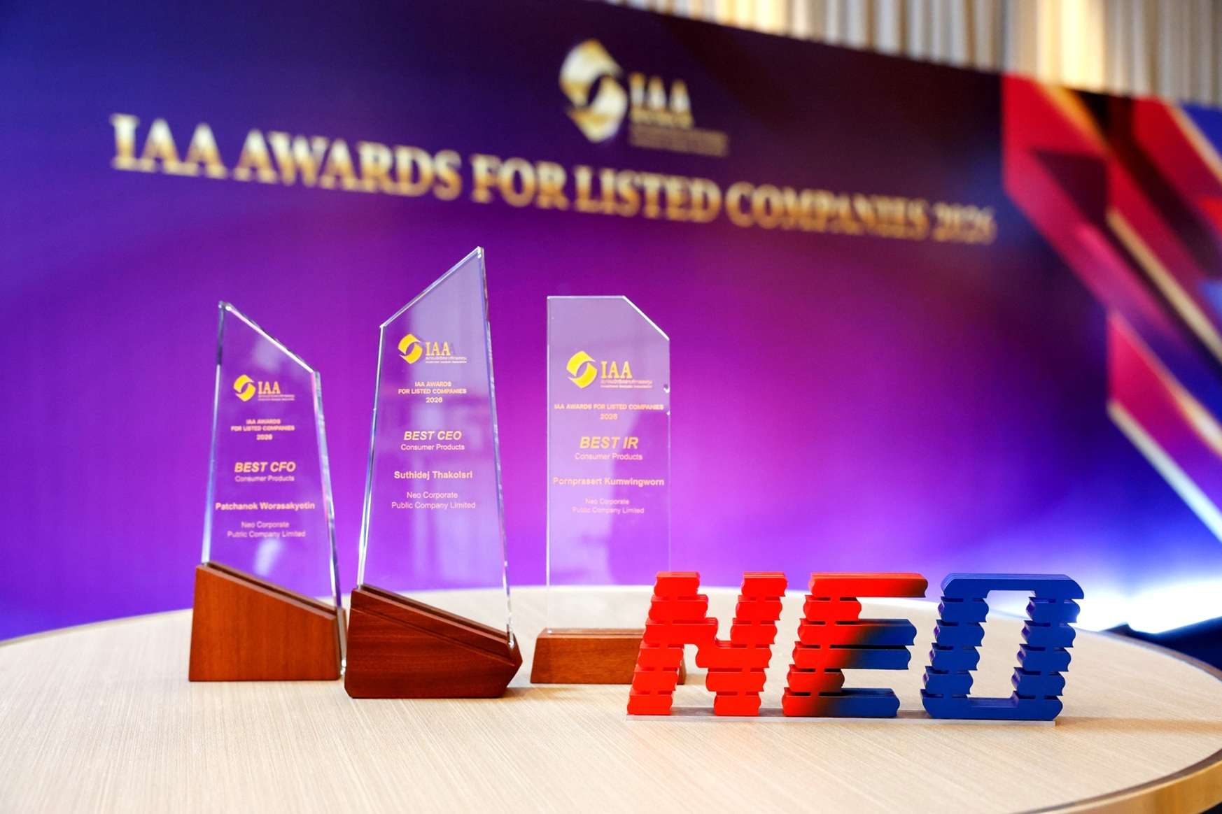 ภาพโล่รางวัลอะคริลิกใส 3 รางวัล ได้แก่ BEST CEO, BEST CFO และ BEST IR จากงาน IAA Awards for Listed Companies 2026 ตั้งเรียงกันด้านหลังโลโก้ NEO แบบสามมิติสีแดงและสีน้ำเงิน