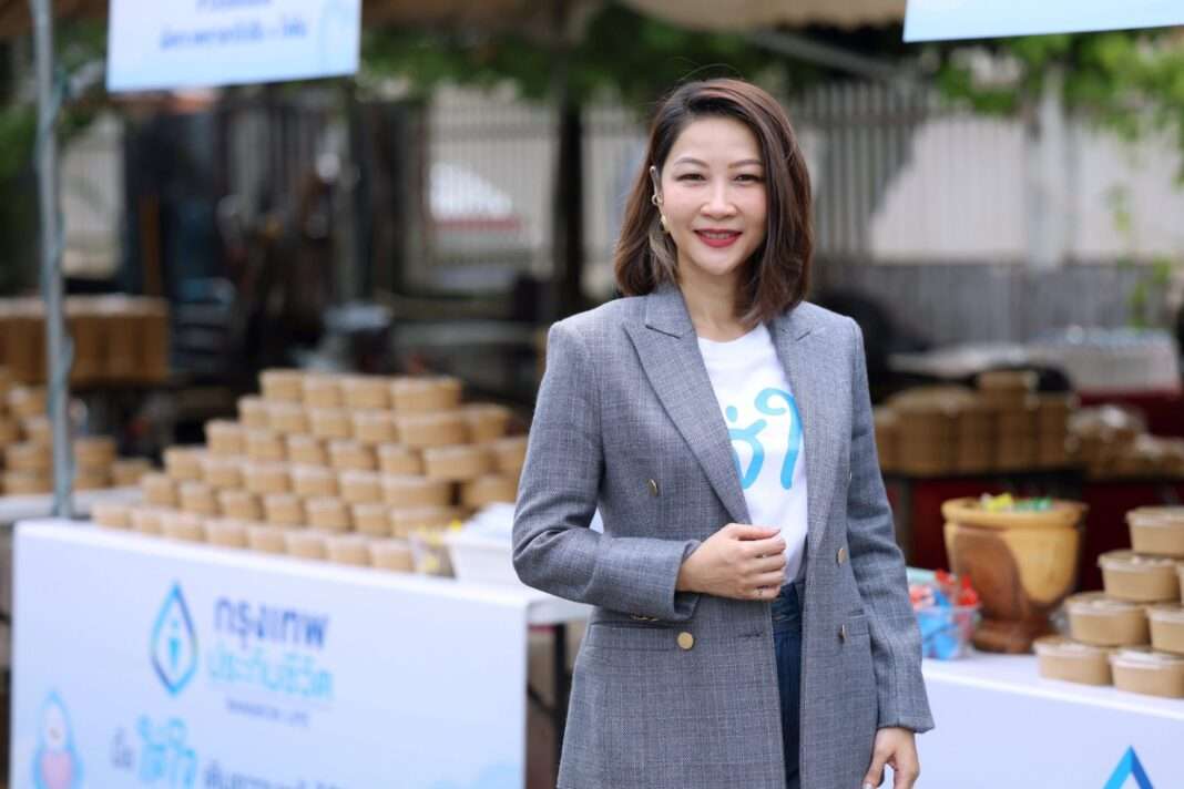Oranart-Nachaphong-Bangkok-Life-Assurance-Meal-Donation-Mirror-Foundation คุณอรนาฎ นชะพงษ์ ผู้ช่วยผู้จัดการใหญ่ สายกลยุทธ์การตลาดและบริหารจัดการลูกค้า กรุงเทพประกันชีวิต สวมเสื้อสูทสีเทายืนยิ้มด้วยความอบอุ่น บริเวณจุดส่งมอบอาหารโครงการมื้อใส่ใจ เติมความหวังให้ชีวิต โดยมีกล่องอาหารจัดเตรียมไว้อยู่เบื้องหลัง