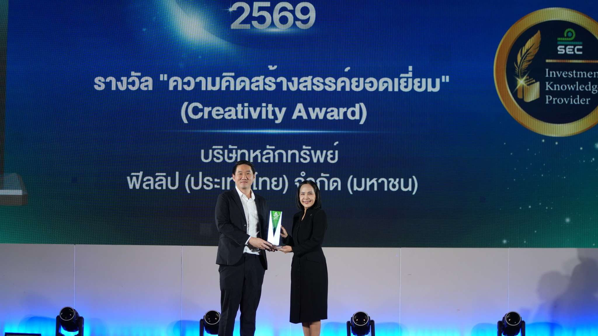นายสานุพงศ์ สุทัศน์ธรรมกุล ขึ้นรับมอบถ้วยรางวัล ความคิดสร้างสรรค์ยอดเยี่ยม (Creativity Award) บนเวที จากผู้บริหารสำนักงาน ก.ล.ต. ในงานส่งเสริมความรู้ด้านการลงทุนประจำปี 2569
