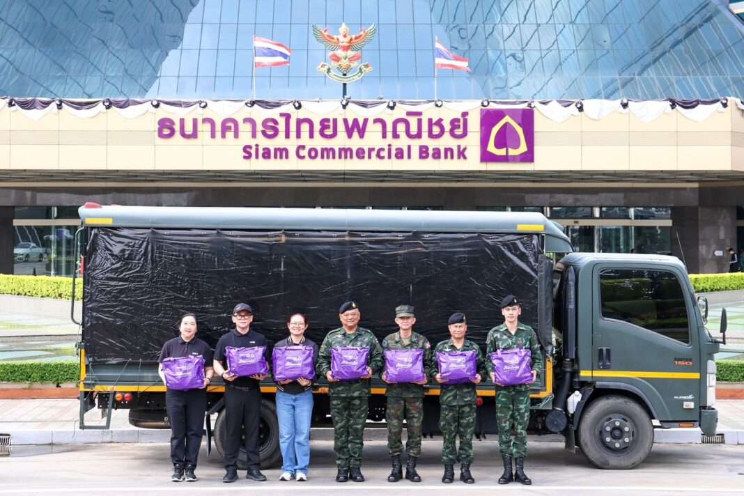 SCB-Executives-And-Military-Officers-Handover-Relief-Bags ผู้บริหารธนาคารไทยพาณิชย์ร่วมกับเจ้าหน้าที่ทหารระดับสูงจากกองบัญชาการกองทัพไทย ยืนถ่ายภาพร่วมกันพร้อมถือถุงยังชีพสีม่วง น้ำใจไทยพาณิชย์ บริเวณด้านหน้าอาคารสำนักงานใหญ่ ธนาคารไทยพาณิชย์