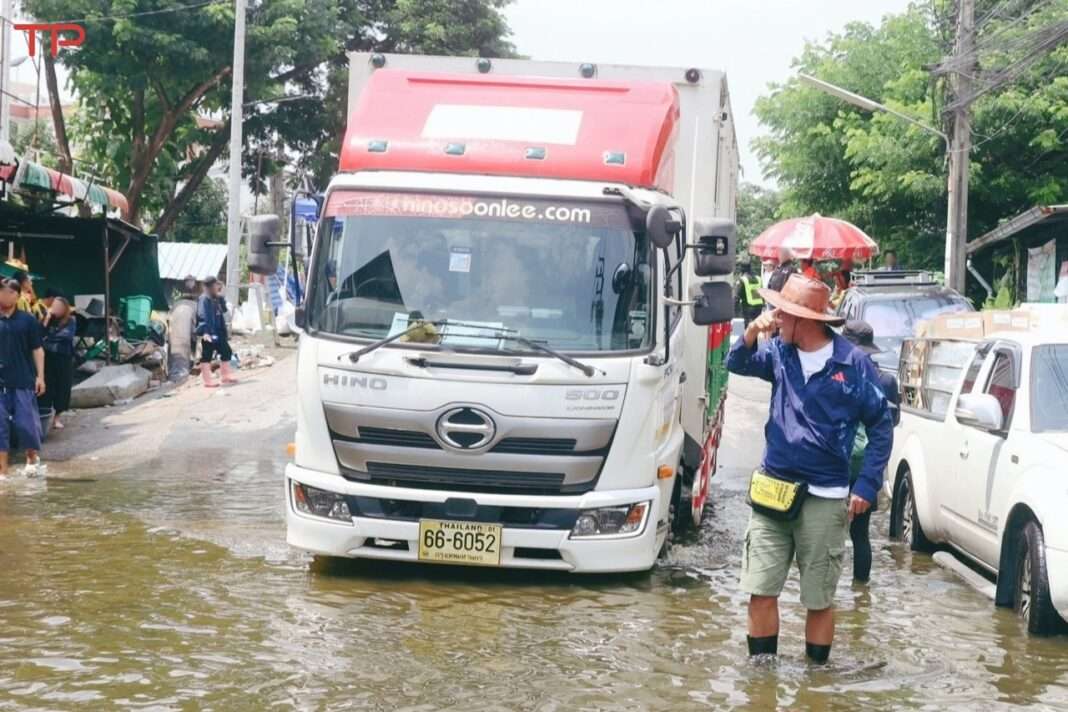 TPLL-Truck-Delivering-Flood-Relief-Supplies รถบรรทุกหกล้อของบริษัท ไทยพาร์เซิล โลจิสติกส์ จำกัด (TPLL) ขับลุยน้ำท่วมบนถนนเพื่อนำสิ่งของบริจาคไปช่วยเหลือผู้ประสบอุทกภัย โดยมีประชาชนเดินลุยน้ำอยู่บริเวณใกล้เคียง