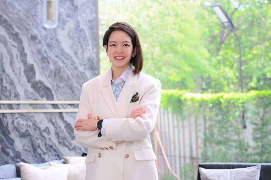 Umaporn-Thanyaklakpark-SENA-Development-Campaign นางสาวอุมาพร ธัญลักษณ์ภาคย์ ผู้อำนวยการอาวุโส สายงาน Corporate Marketing บริษัท เสนาดีเวลลอปเม้นท์ จำกัด (มหาชน) หรือ SENA สวมเสื้อสูทสีขาว ยืนกอดอกส่งรอยยิ้มอย่างมั่นใจ ท่ามกลางบรรยากาศพื้นที่ส่วนกลางของโครงการที่อยู่อาศัยที่ตกแต่งอย่างหรูหรา