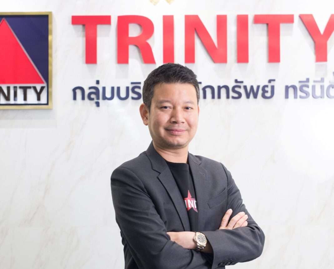 ดร.วีรพัฒน์ เพชรคุปต์ ประธานเจ้าหน้าที่บริหาร บริษัทหลักทรัพย์ ทรีนีตี้ จำกัด สวมชุดสูทสากลยืนกอดอกด้วยความมั่นใจ บริเวณหน้าป้ายโลโก้กลุ่มบริษัทหลักทรัพย์ ทรีนีตี้