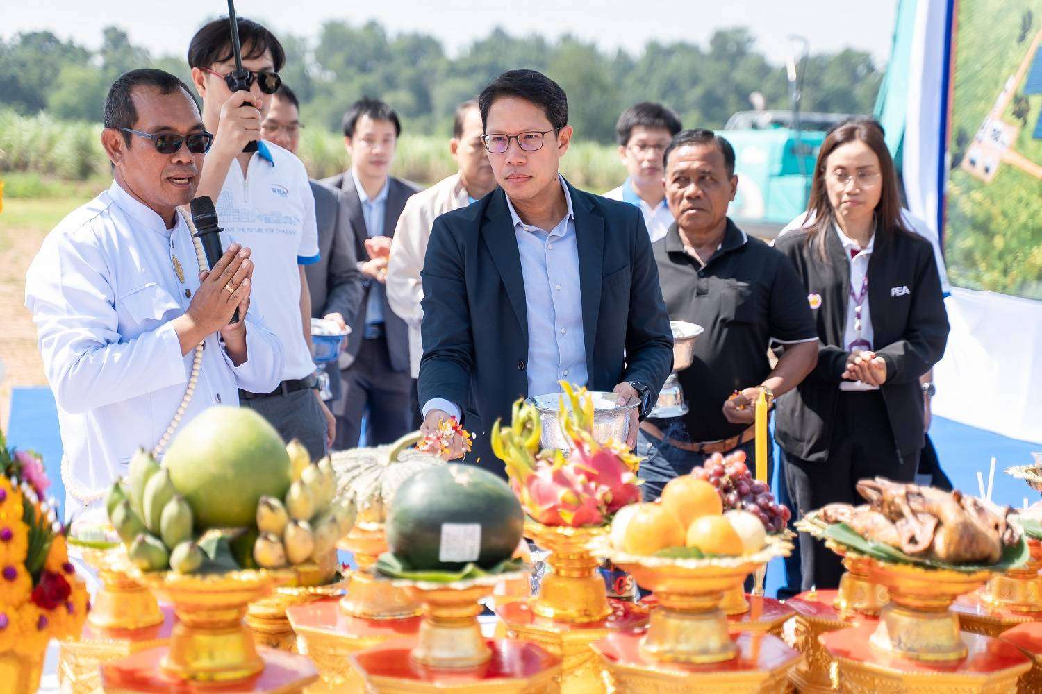ภาพนายอัครินทร์ ประเทืองสิทธิ์ ประธานเจ้าหน้าที่บริหาร บริษัท ดับบลิวเอชเอ ยูทิลิตี้ส์ แอนด์ พาวเวอร์ จำกัด (มหาชน) หรือ WHAUP กำลังประกอบพิธีโปรยดอกไม้มงคลบนโต๊ะบวงสรวงที่มีผลไม้และเครื่องเซ่นไหว้ เพื่อเริ่มโครงการก่อสร้างโรงไฟฟ้าพลังงานแสงอาทิตย์ โดยมีผู้แทนจาก กฟภ. องค์กรปกครองส่วนท้องถิ่น และคณะผู้บริหารยืนร่วมพิธีอยู่ด้านหลัง