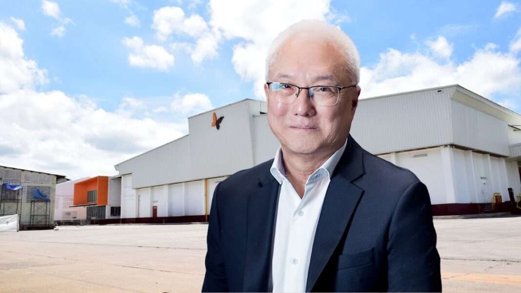 Weerachai-Mansinthorn-CEO-TIPAK-Factory นายวีรชัย มั่นสินธร ประธานเจ้าหน้าที่บริหาร บริษัท อุตสาหกรรมไทยบรรจุภัณฑ์ จำกัด (มหาชน) หรือ TIPAK สวมเสื้อเชิ้ตสีขาวทับด้วยสูทสีกรมท่า ยืนถ่ายภาพด้วยรอยยิ้มอยู่ด้านหน้าอาคารโรงงานผลิตบรรจุภัณฑ์